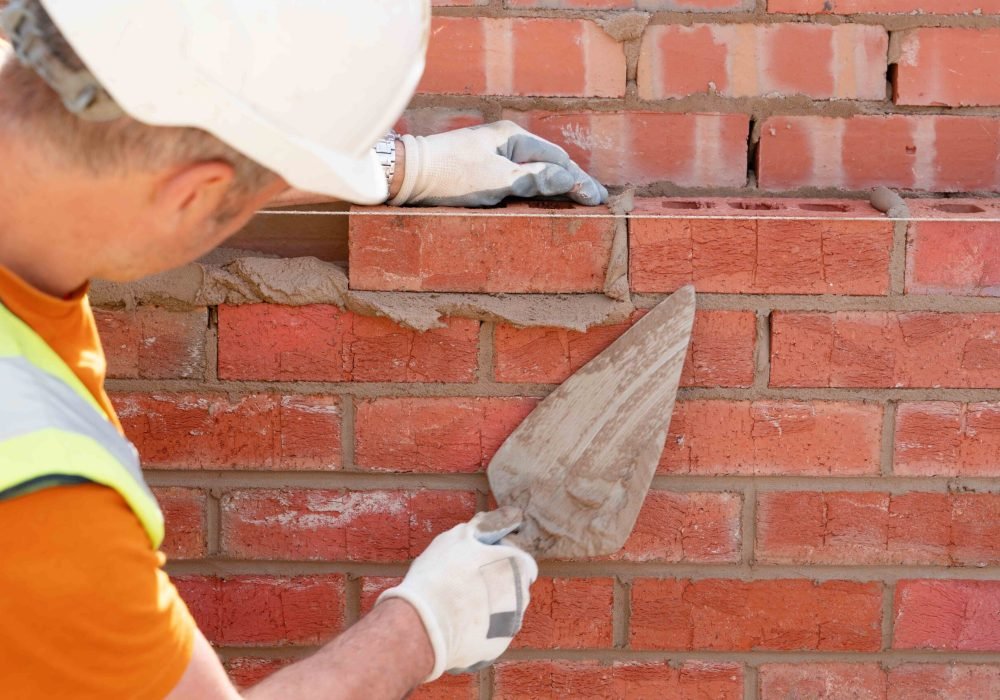 Bricklayer laying bricks on mortar on new residential house construction. Get NVQ in bricklaying